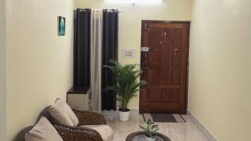 A hallway with a wicker sofa, a potted plant, a door, and a wall-mounted clock.