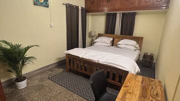 A bedroom with a bed, a desk, a chair, a ceiling fan, a potted plant, and a wall-mounted air conditioner.