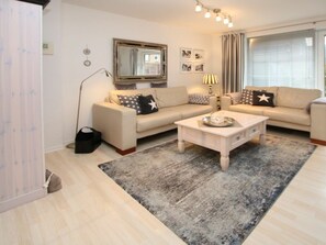Ein modernes Wohnzimmer mit zwei Sofas, einem Couchtisch, einer Stehlampe und einem großen Fenster mit Vorhängen.