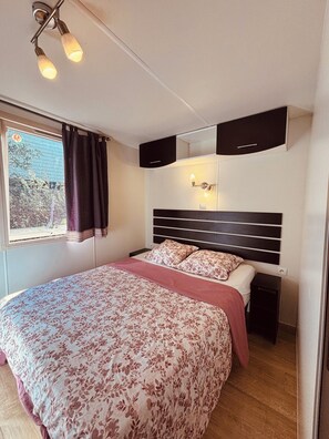 Ein Schlafzimmer mit einem Bett, einem Nachttisch, einem Spiegel und einem Fenster mit Vorhängen.