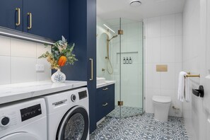 Een moderne badkamer met een wasmachine, een douchecabine van glas en vloertegels met een patroon.