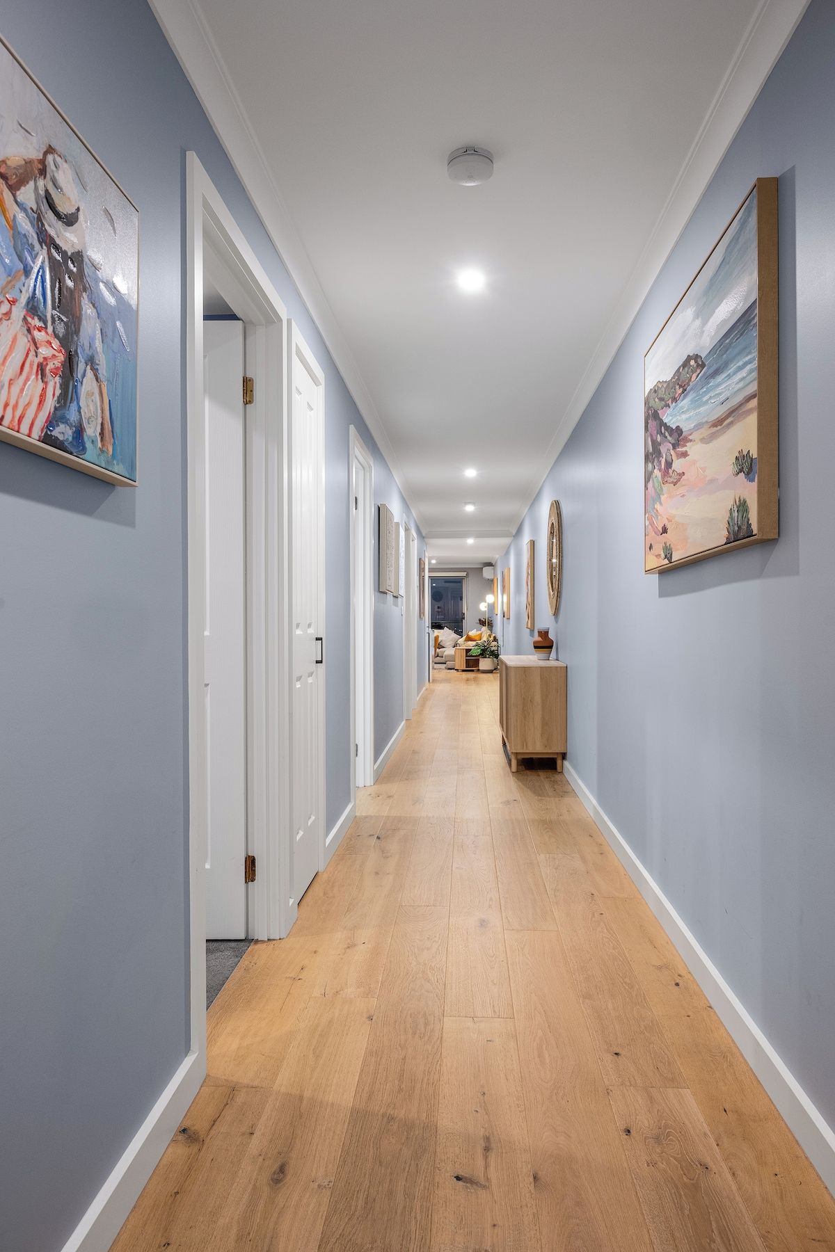 A hallway with wooden flooring, white walls, and artwork on the walls.