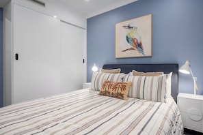 A bedroom with a bed, pillows, a nightstand, a lamp, and a wall-mounted painting. - Beachfront 3BR Retreat w Parking, Pool and Tennis (Saint Kilda West)