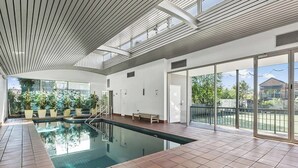 Una piscina interior con vistas despejadas al exterior, techo de madera y un banco.