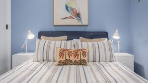 Un dormitorio con cama, almohadas, cabecera, mesitas de noche y un cuadro en la pared.