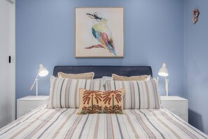 Een slaapkamer met een bed, kussens, een hoofdbord, nachtkastjes en een aan de muur hangend schilderij.