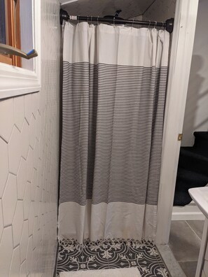 A bathroom with a shower curtain, a patterned floor, and a white wall with a hexagonal design. - Cozy 2-bedroom Beach Bungalow in lovely Ocean Grove, NJ with AC (Neptune Township)