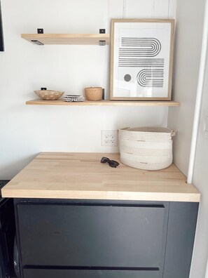A kitchen with a wooden countertop, a framed abstract artwork, and a woven basket.