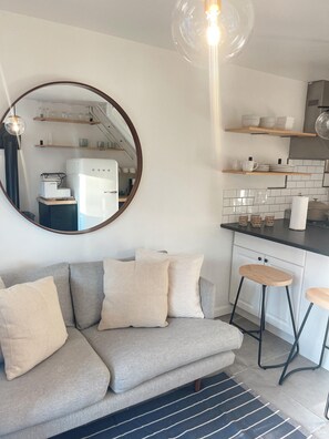 A modern kitchen with white cabinets, a black countertop, and a round mirror above a grey sofa with striped cushions.