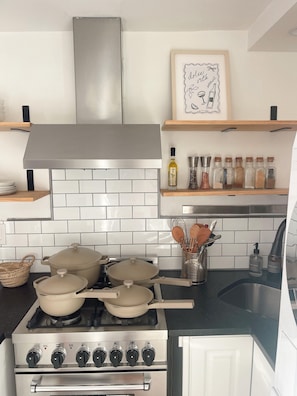 A modern kitchen with a stainless steel stove, white tiled backsplash, and wooden shelves above holding kitchen items and spices.