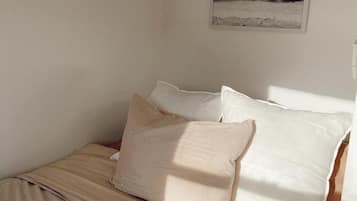 A bed with a beige bedspread and pillows, a framed picture of a beach scene on the wall, and a window allowing natural light into the room.