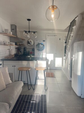 A modern kitchen with a central island, bar stools, a washing machine, and a staircase leading to an upper level. - Cozy 2-bedroom Beach Bungalow in lovely Ocean Grove, NJ with AC (Neptune Township)