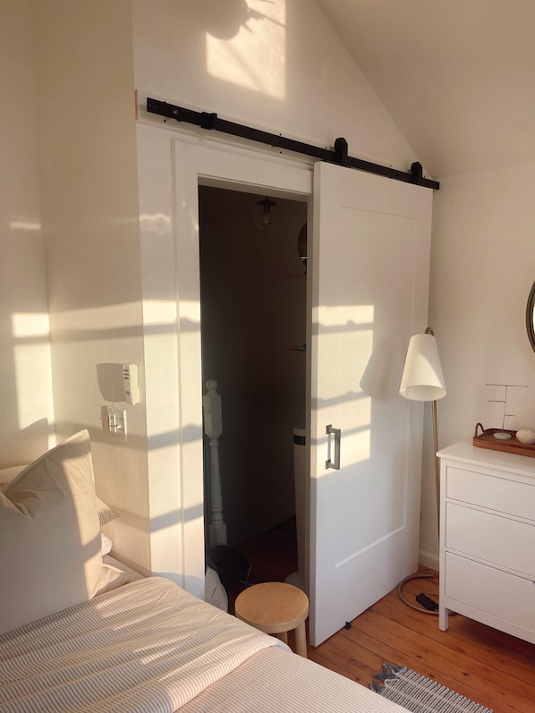 A bedroom with a bed, bedside table, lamp, and a door leading to another room.