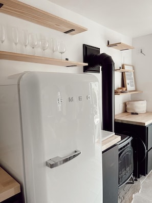 A modern kitchen with a white refrigerator, wooden shelves, a black range hood, and a small television.
