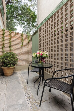 A small outdoor seating area with a table and chairs, a potted plant, and a decorative wall. - Zaterra: Ground-Floor Loft with Private Patio in Roma Norte (Ciudad de México)