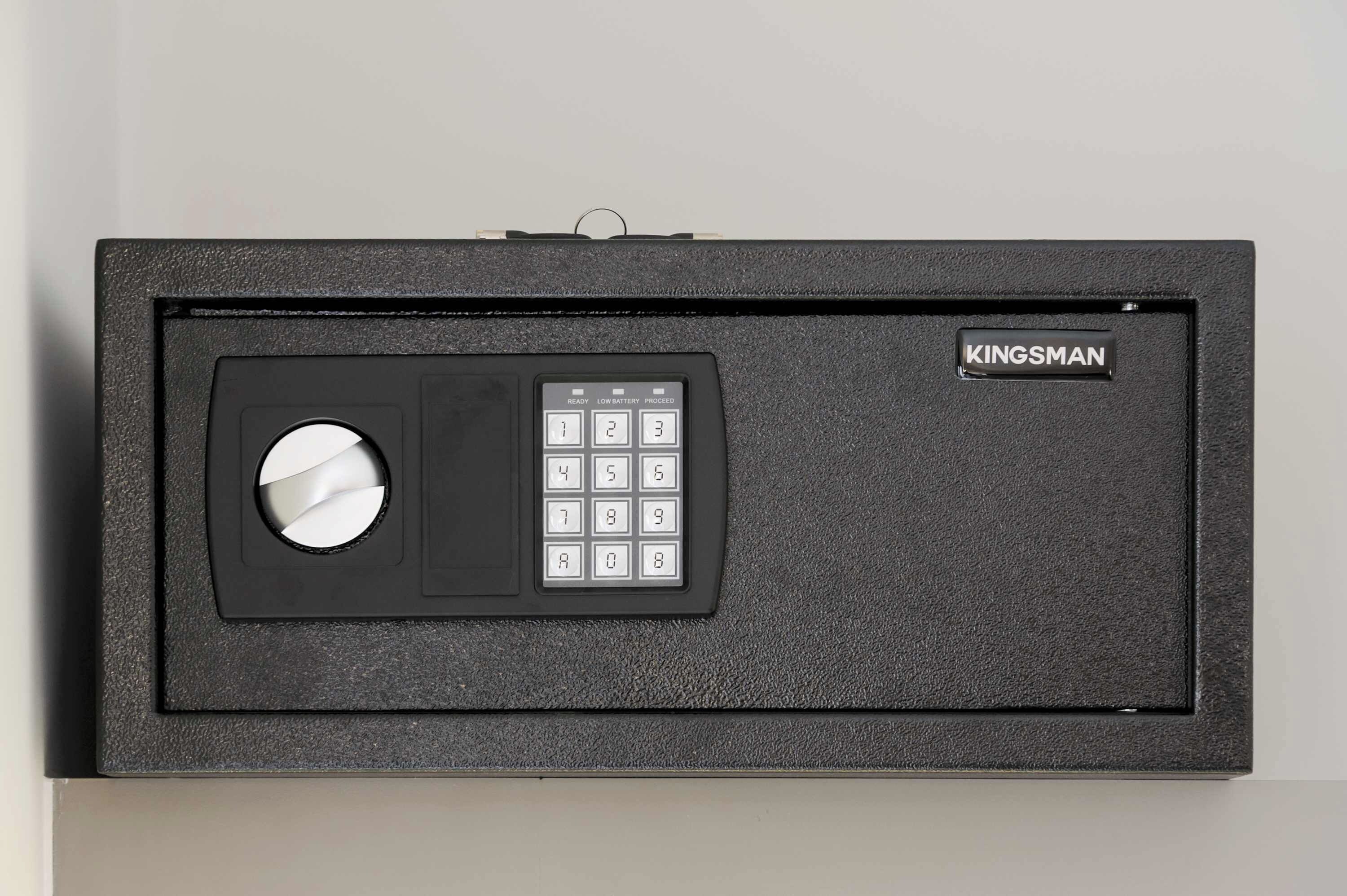 Ein schwarzer Safe mit Tastatur und rundem Schließmechanismus, beschriftet mit 'KINGSMAN'.