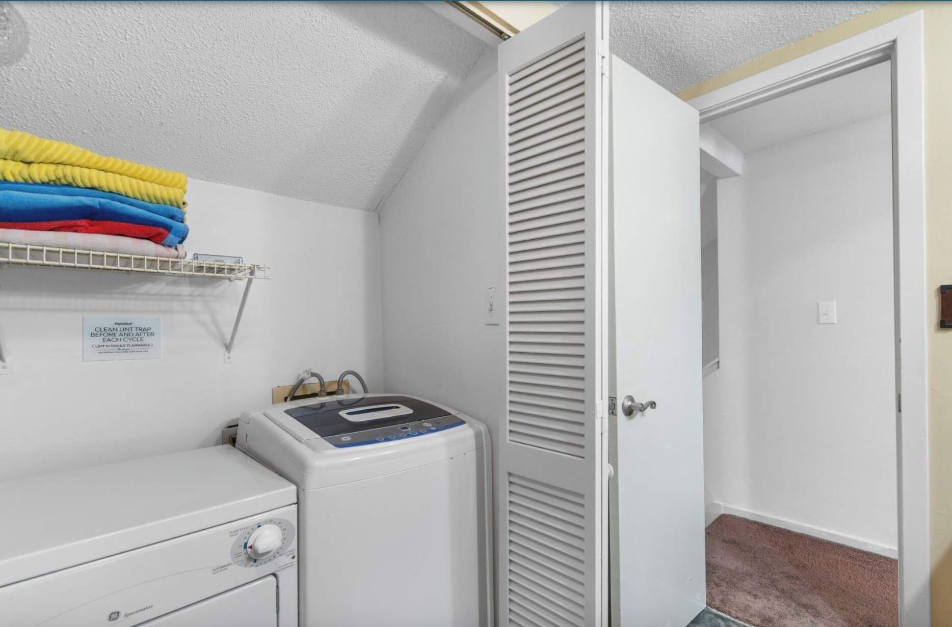 A laundry area with a washing machine, a drying rack with folded clothes, and a closed door.