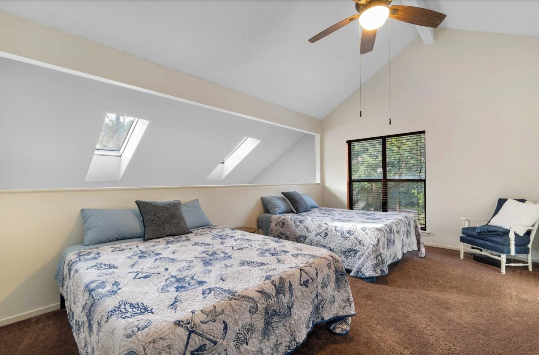 A bedroom with two beds, a ceiling fan, skylights, and a window with blinds.