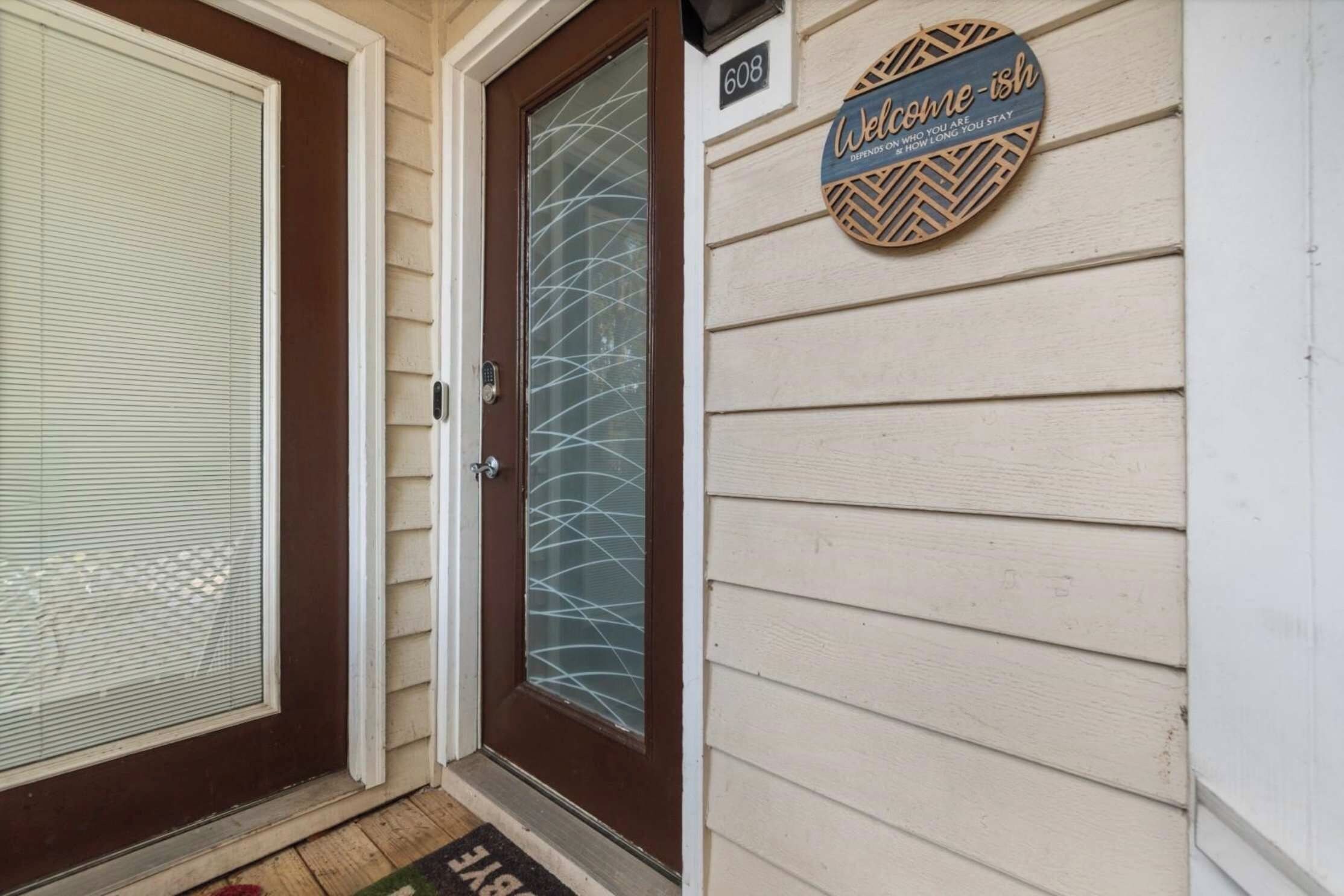 A house entrance with a brown door, a glass door with a metal handle, and a welcome sign on the wall.