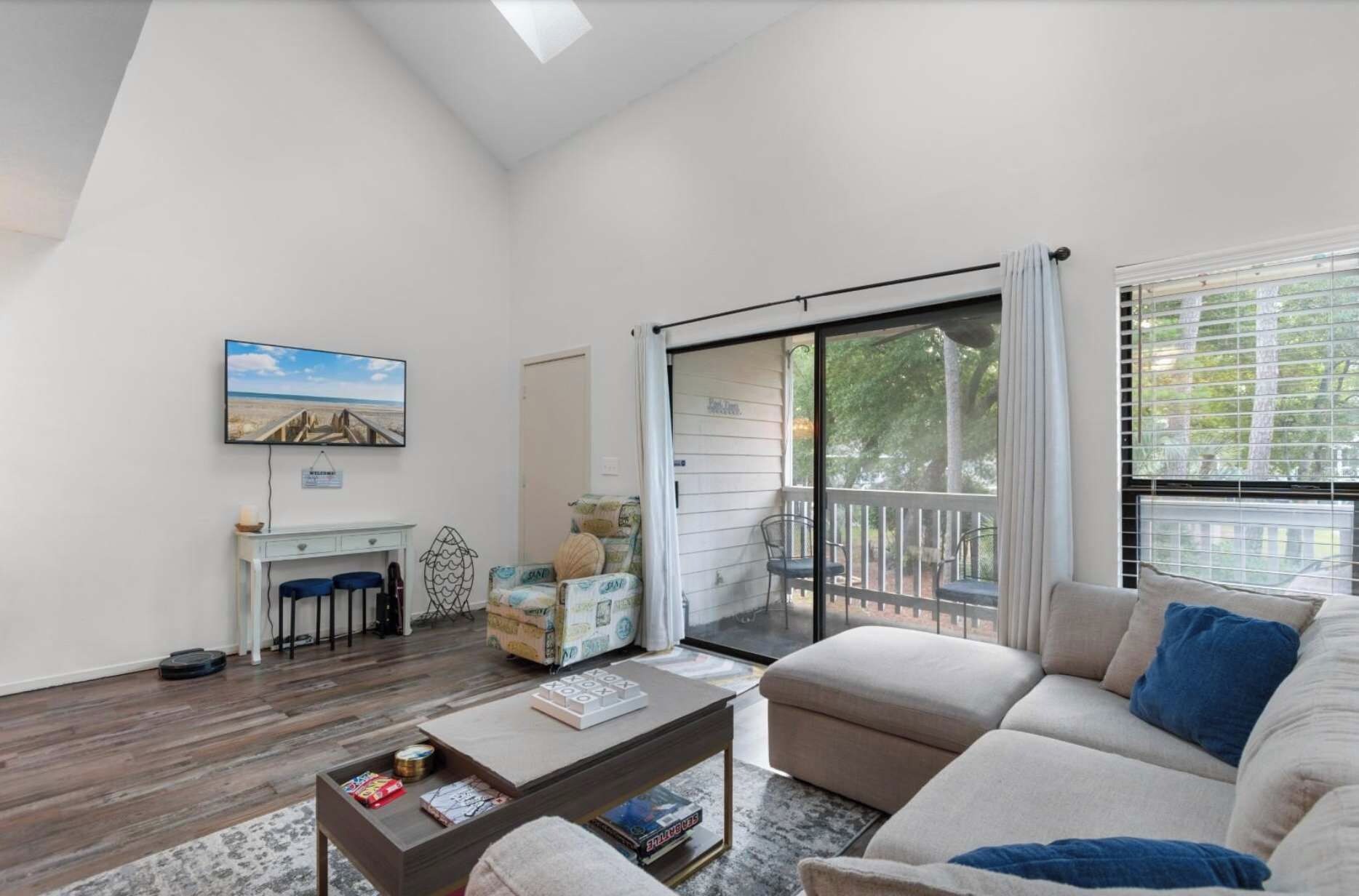 A spacious living room with a large sofa, a coffee table, and a television mounted on the wall.