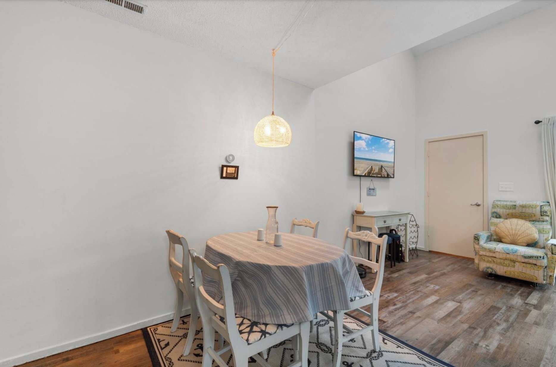 Un comedor con una mesa redonda, sillas, una lámpara colgante, un televisor en la pared y una puerta.