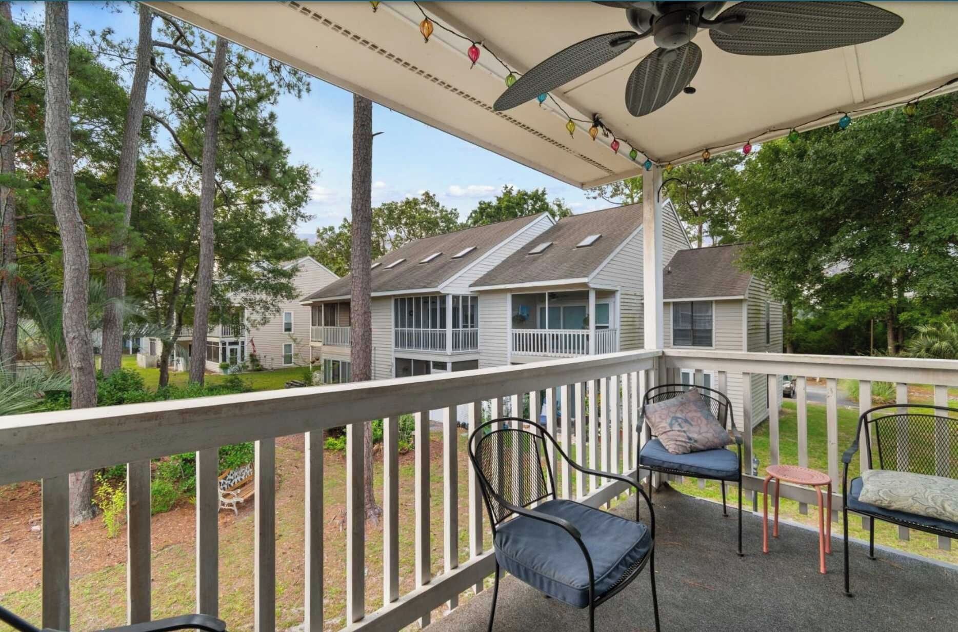 A covered outdoor area with a railing, chairs, and a ceiling fan.