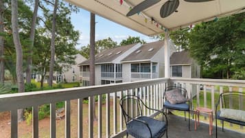A covered outdoor area with a railing, chairs, and a ceiling fan.