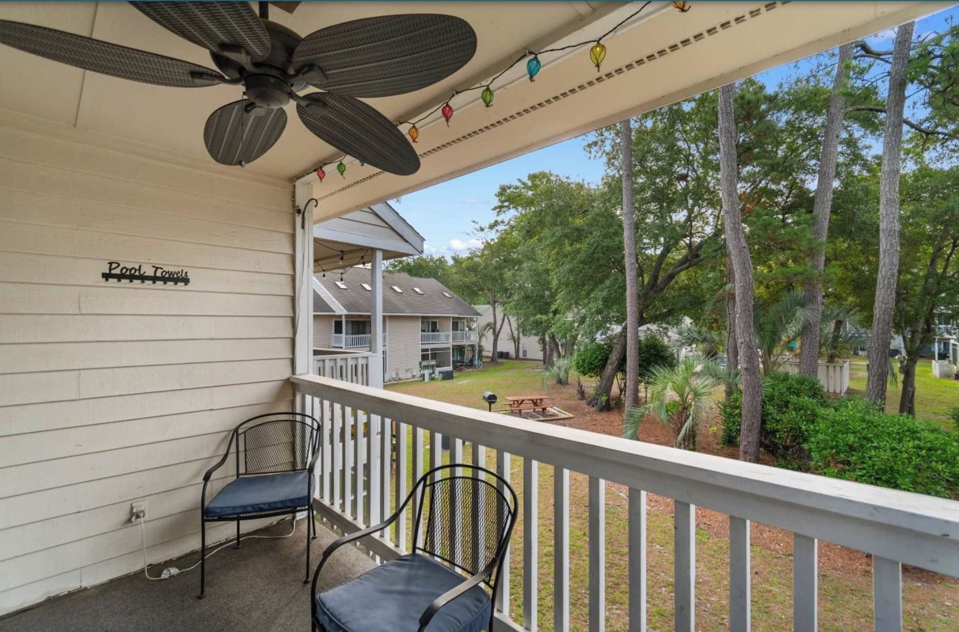 A covered outdoor area with two chairs, a ceiling fan, and a sign reading 'Pool Towels'.