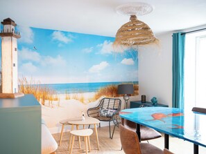 Een kamer met een strandmuurschildering, een tafel, stoelen en een hanglamp.