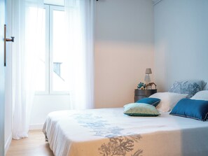 Een slaapkamer met een bed, een nachtkastje, een lamp en een raam met gordijnen.