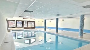 Una piscina interna con acqua cristallina, pareti piastrellate e una combinazione di colori blu e bianco.