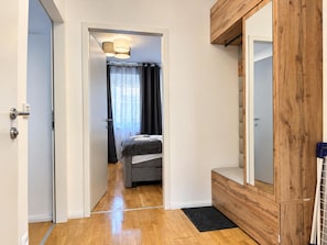 Habitación de hotel con un armario de madera, una cama con colchón gris, una pequeña zona de estar y una puerta que da a otra habitación.