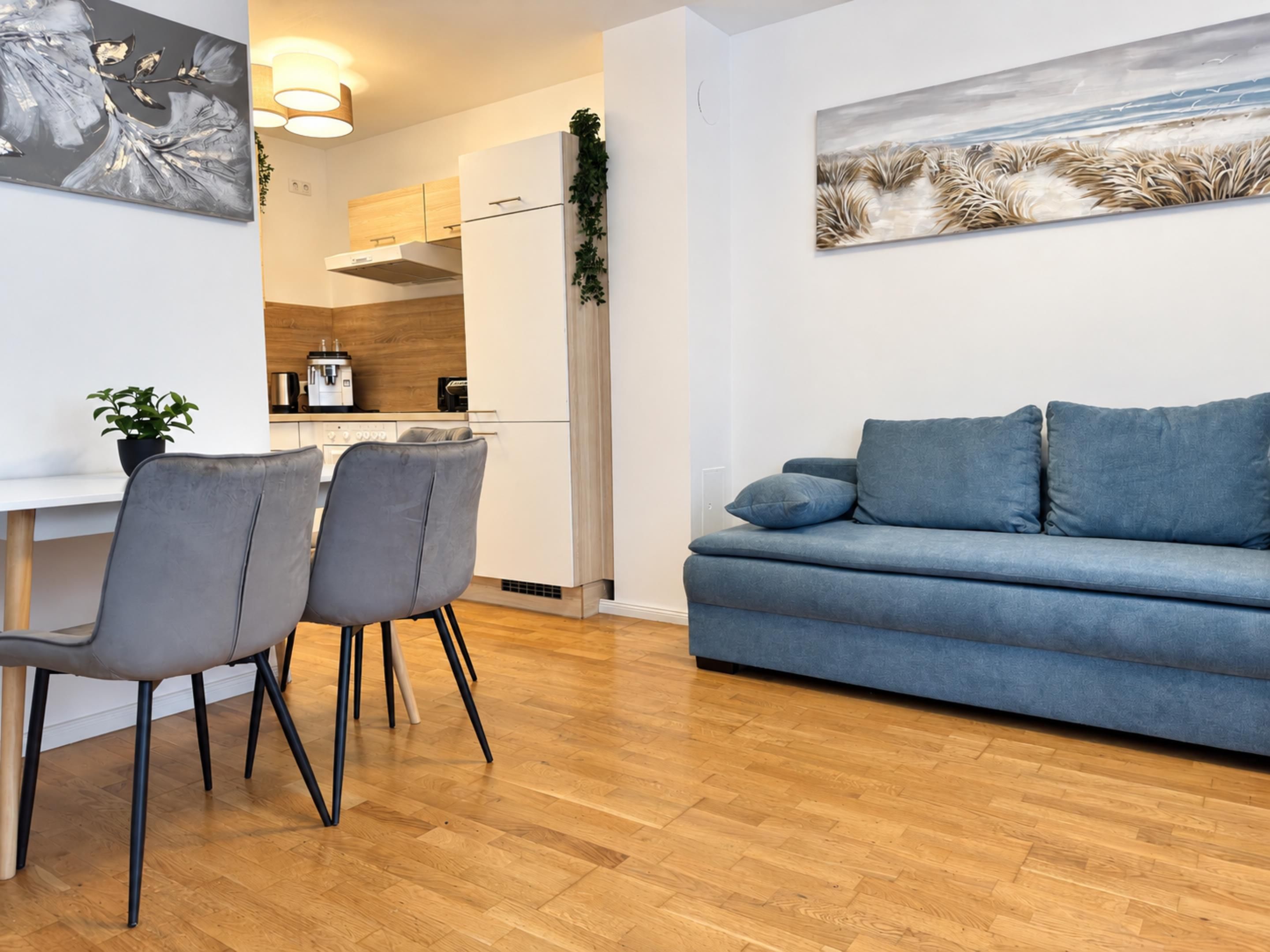 Una sala moderna con un sofá azul, dos sillas grises y suelo de madera.