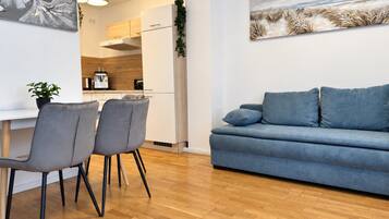 Una sala moderna con un sofá azul, dos sillas grises y suelo de madera.