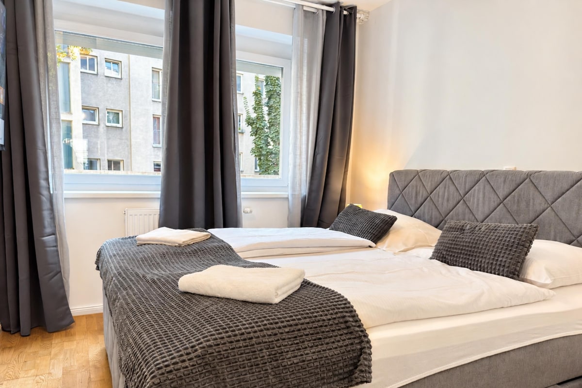 A hotel room with a bed, curtains, and a window with a view of buildings.