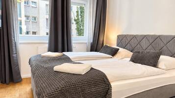 A hotel room with a bed, curtains, and a window with a view of buildings.