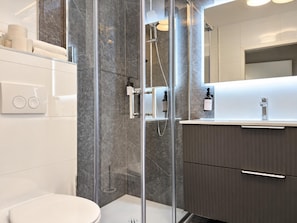 Un baño moderno con ducha envuelta en vidrio, un inodoro y un lavamanos con espejo.