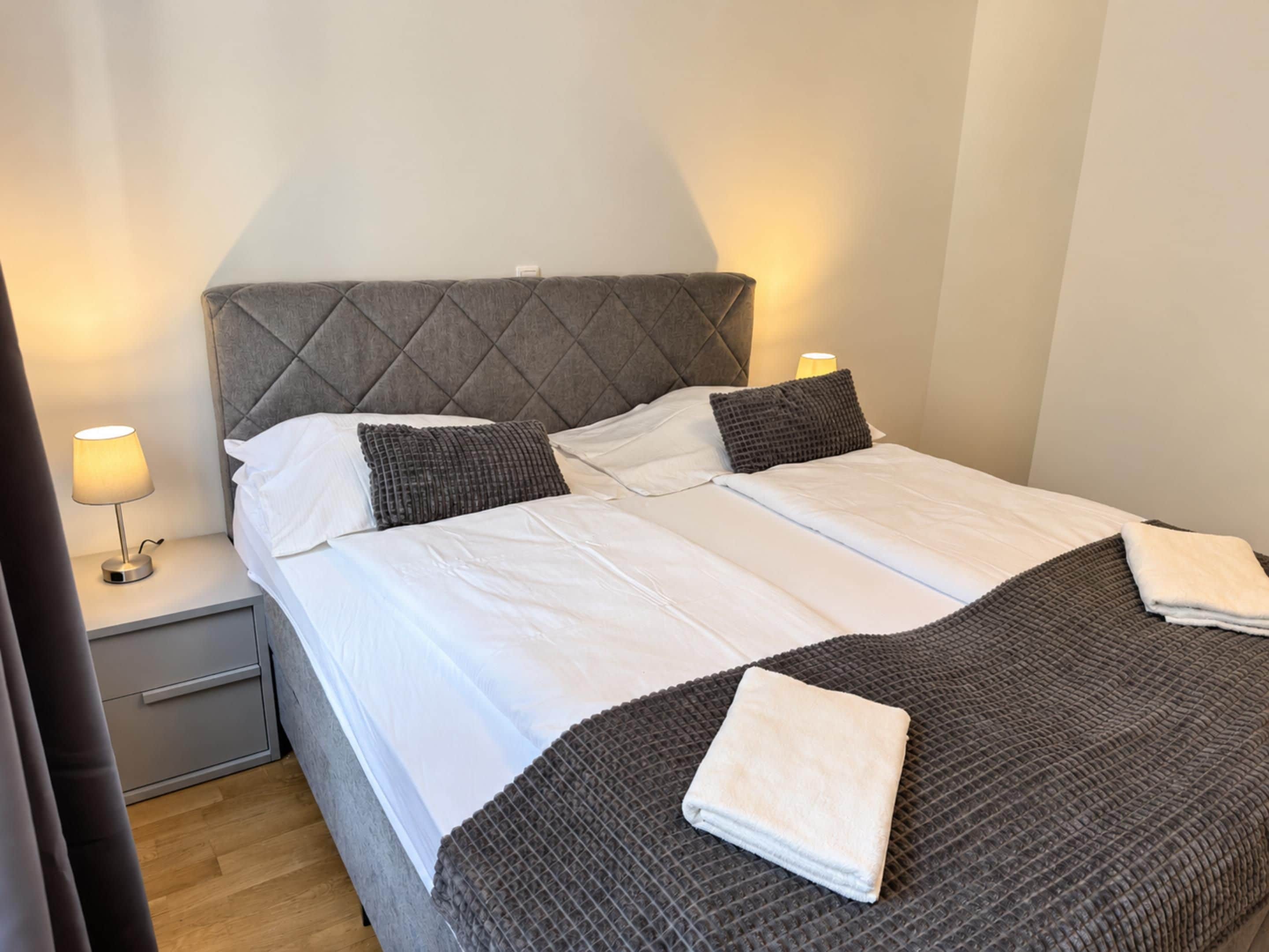 A double bed with a grey headboard, white linens, and a grey textured blanket.