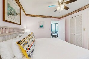 Un dormitorio con cama, ventilador de techo, un cuadro en la pared y una puerta que da a otra habitación.