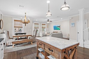 Un vaste espace de vie comprenant une table à manger, un lustre et une grande fenêtre équipée de stores.