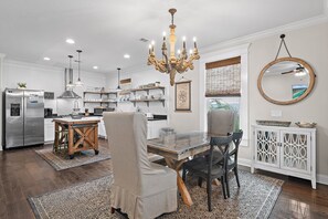 Une cuisine moderne avec un coin repas, agrémentée d’un lustre, de meubles blancs et d’un grand miroir.