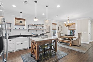 Une cuisine moderne avec des meubles blancs, une table à manger en bois et des luminaires suspendus.