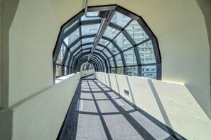Ein Korridor mit Glasdecke und Metallkonstruktion, der zu einem mehrstöckigen Gebäude führt.