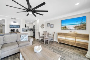 Ein modernes Wohnzimmer mit Deckenventilator, einer Kaffeebar und einem Gemälde zum Thema Strand.