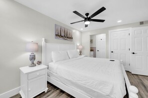 Ein Schlafzimmer mit Bett, Nachttischen, Deckenventilator und weißen Türen.