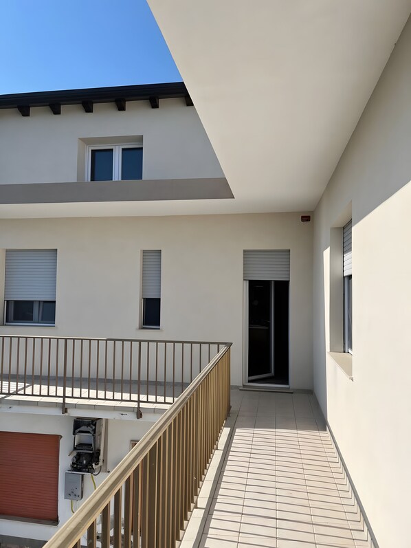A modern building with a flat roof, a balcony with a metal railing, and a tiled floor.
