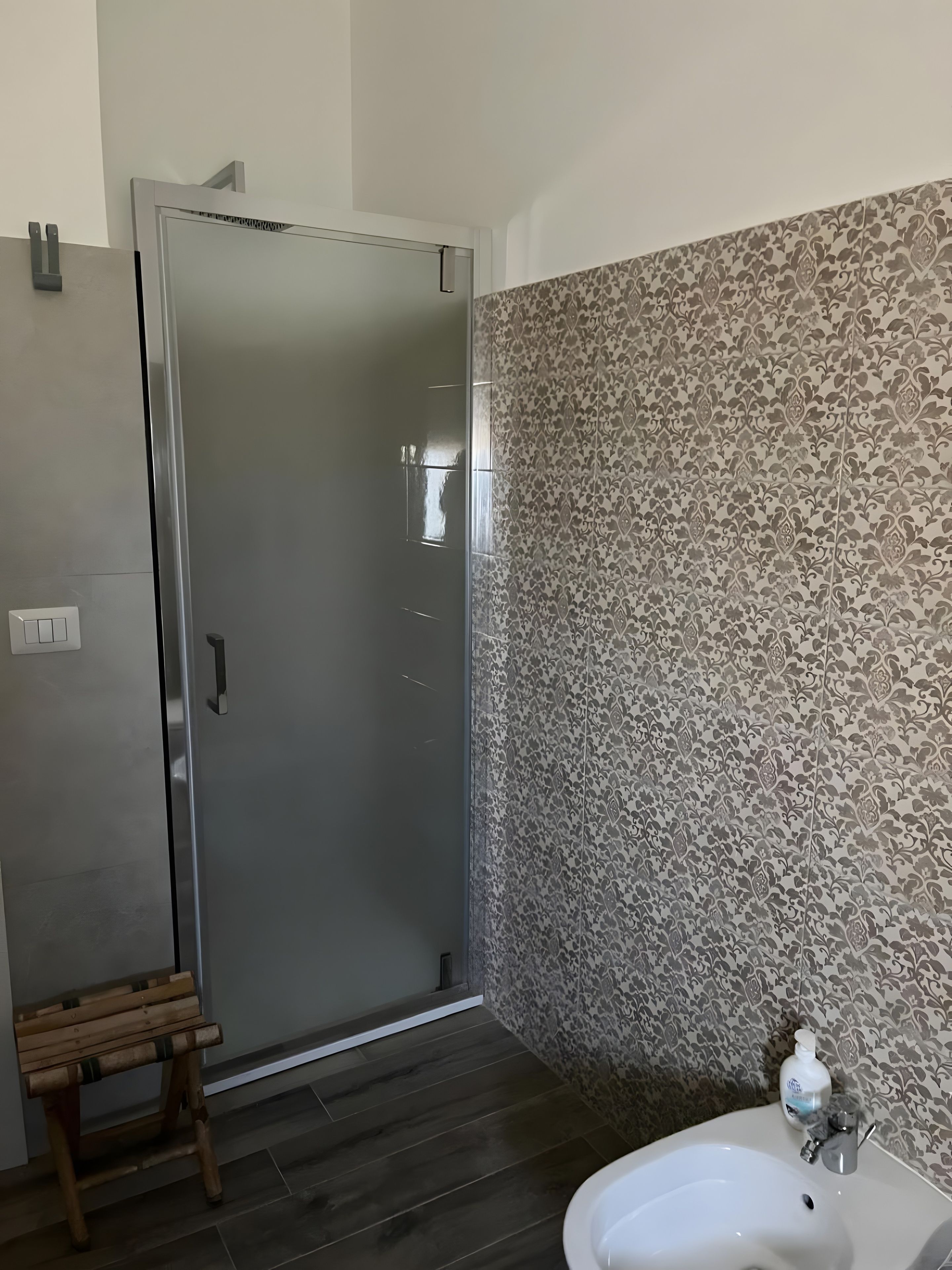 A bathroom with a shower, a wooden bench, a sink, and patterned wall tiles.