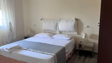 Un letto rifatto con lenzuola bianche e gonna rosa, due comodini con lampade e una finestra con tende trasparenti.