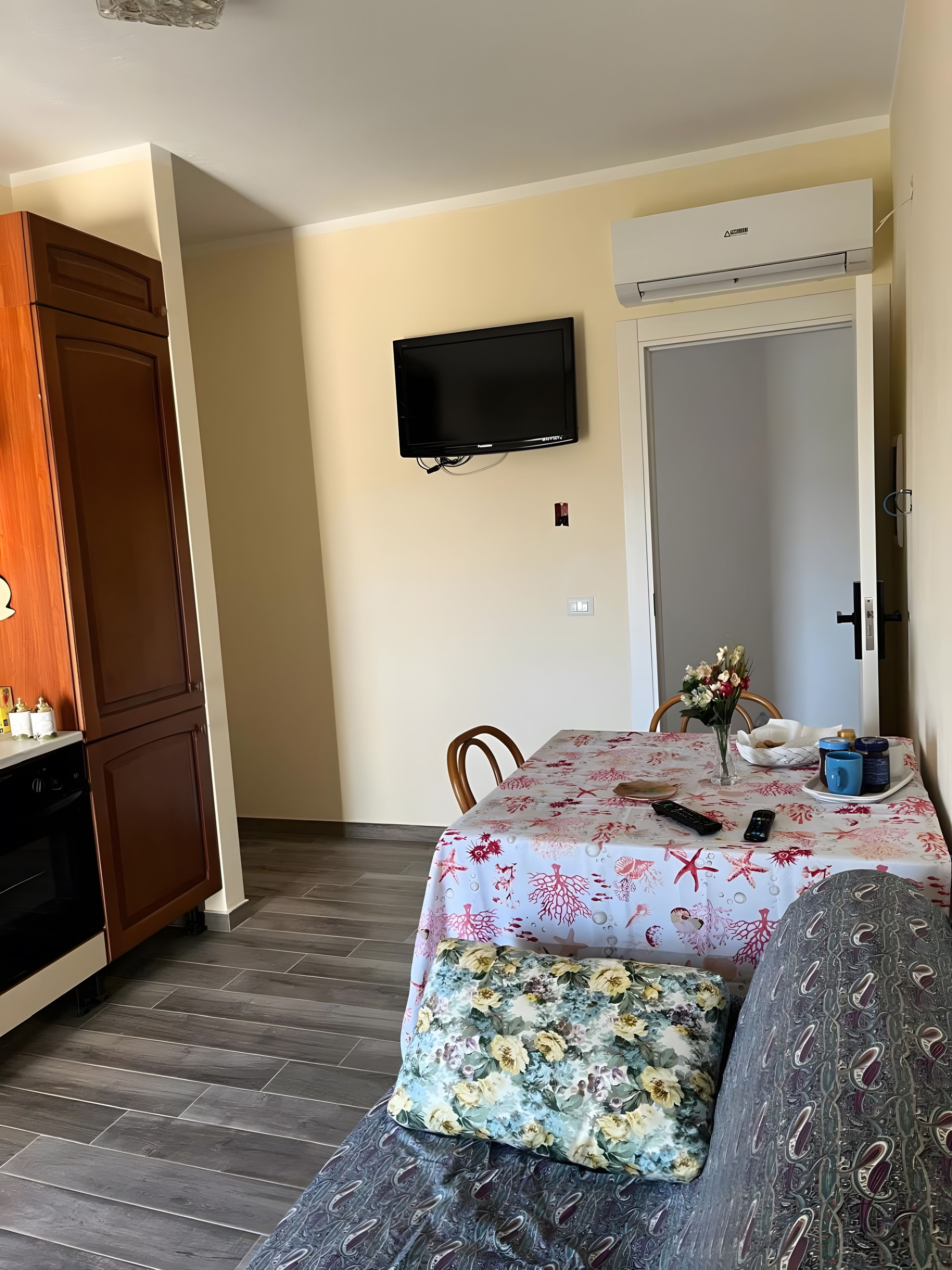 Una stanza con un tavolo da pranzo, un divano, una TV a parete e angolo cottura.