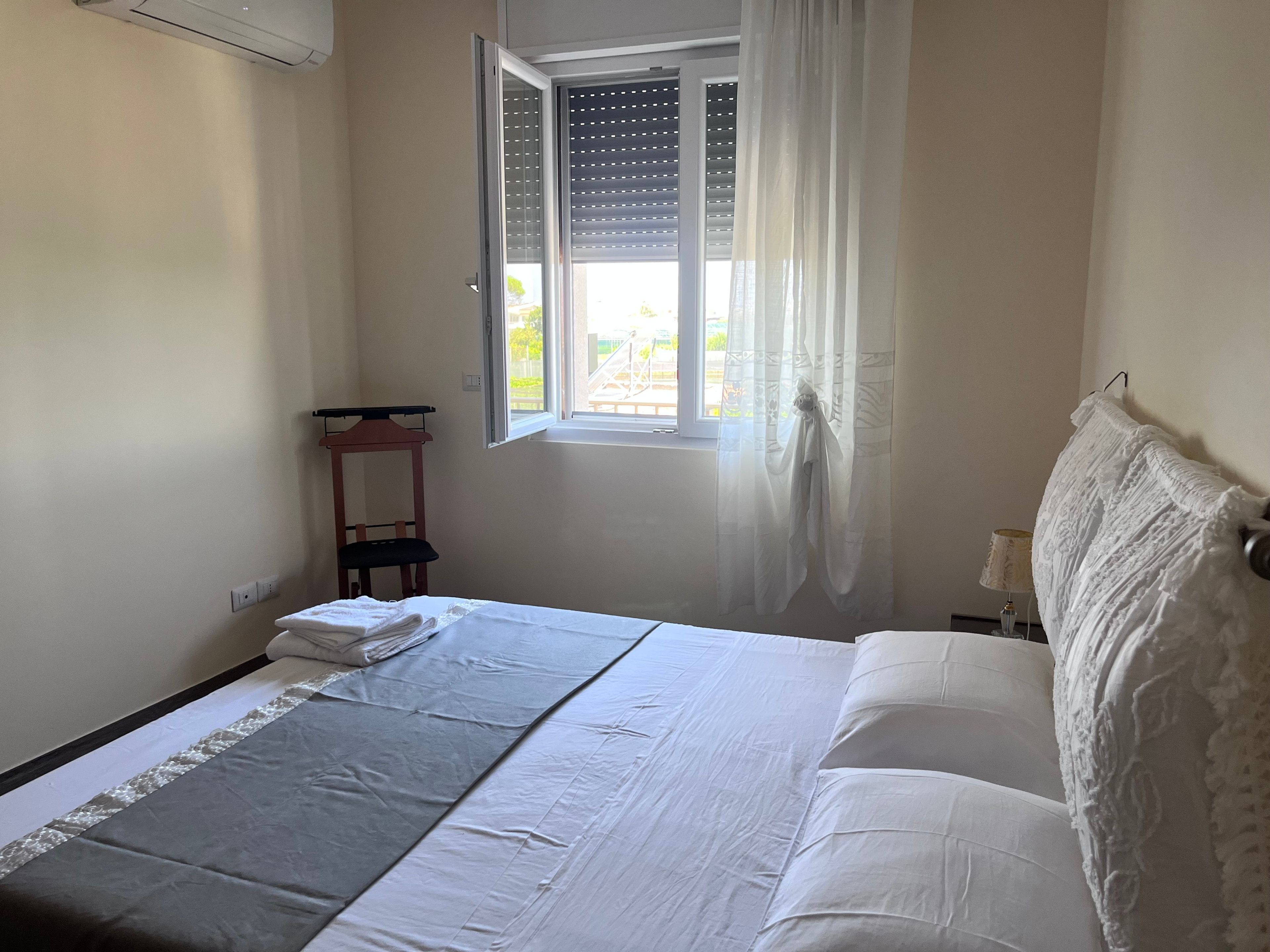 Een slaapkamer met een bed, een raam met jaloezieën, een stoel en een lamp.